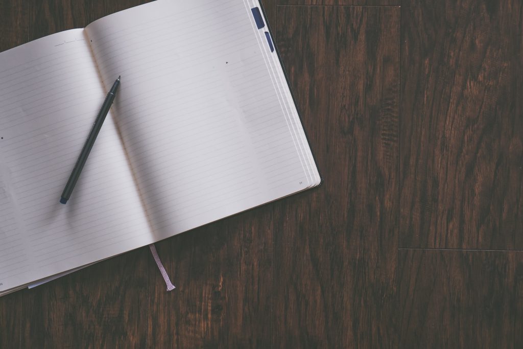 An open lined journal with a black pen resting on its pages, set against a dark wooden surface, ready for writing intentions or shadow work prompts during the Full Moon.