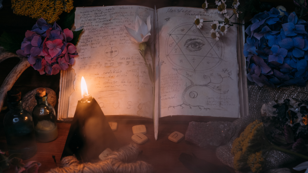 An open grimoire featuring hand-drawn sigils and magical notes, surrounded by a glowing black candle, flowers, and mystical objects. Used to document custom spellwork performed for clients.